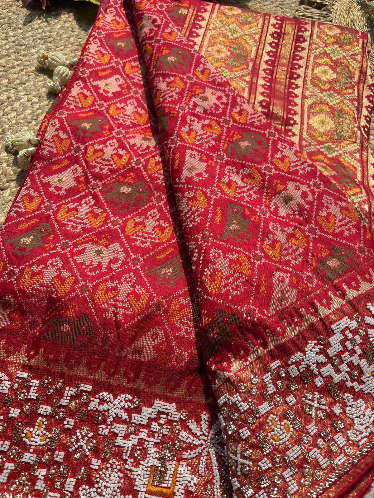 Royal Red Patola-Inspired Designer Saree with Golden Zari-Style Border, Multicolour Floral Motifs, Intricate White Beadwork and Pearl Tassel Detailing